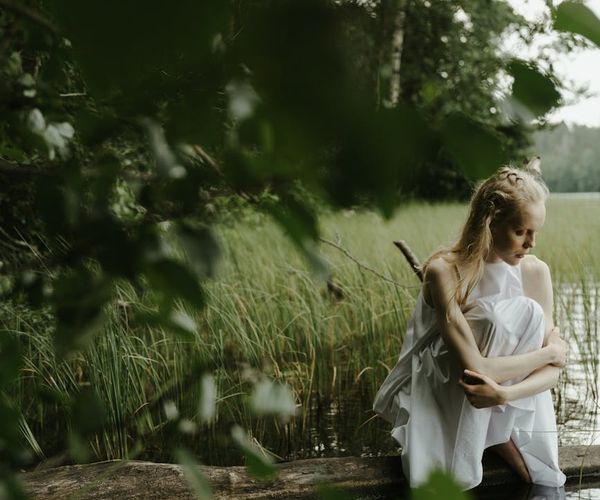 Woman meditating with closed eyes in a peaceful natural setting by the water.